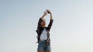 A young woman in casual attire taking a selfie against a clear sky.